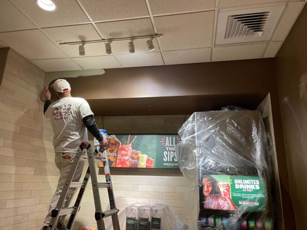 A professional painter meticulously applying fresh paint to a commercial building, ensuring a smooth and even finish.