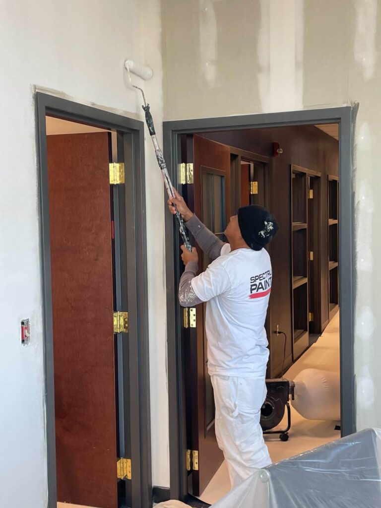 Painter using a roller with an extension pole to paint the upper wall near door frames.