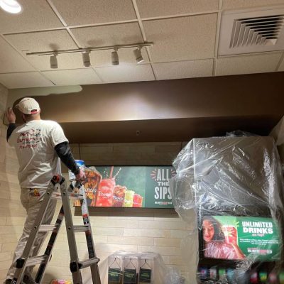 A professional painter meticulously applying fresh paint to a commercial building, ensuring a smooth and even finish.