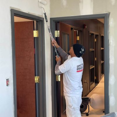 Painter using a roller with an extension pole to paint the upper wall near door frames.